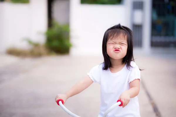 就学前アジアの小さな子供の女の子は遊び心のある顔をします 子供たちは口を包んで自転車に乗る 子供はいい気分で白いドレスを着ていた 夏や春の甘い笑顔 赤ちゃん3歳 — ストック写真