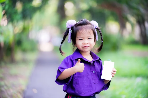 学生アジアの女の子は 青チューブ藁と白いミルクカートンボックスを保持します フルーツジュースの箱を左手で持っている子供 子供は親指と甘い笑顔を示しています 子供たちは紫の制服を着る — ストック写真