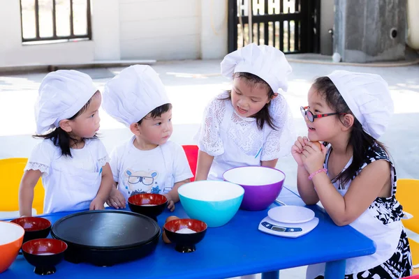幸せなアジアの子供たちの女の子と男の子は白い制服料理と帽子料理を着ています 子供たちはテーブルの横に座り ケーキを作ることに興奮し 決定的な方法について話しました 学びとチームワークの概念 — ストック写真