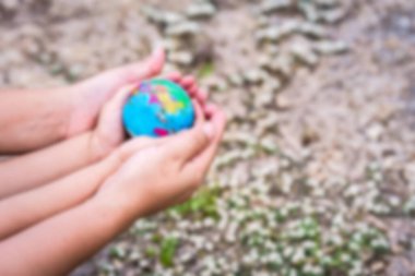 Blurry hands of the mother and child embrace, holding the globe. Background the grass. Concept of love earth, save world. clipart