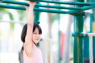 Spor ve sağlık konsepti için çocuk egzersizi. Oyun parkındaki yeşil bir çelik çubukta oynayan ve asılı duran mutlu küçük kız çocuğu. Öğrenci 3-4 yaşlarında..
