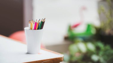 Ahşap bir masanın köşesinde beyaz camlı renkli kalemler. Boşluğu kopyala.