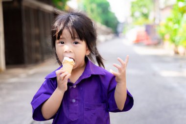 Şirin kız dondurma külahı yiyor. Çocuklar tatlı ve serin yemekten mutludurlar. Mor spor üniforması giyen genç bir öğrenci. 3-4 yaşlarında bir çocuk..