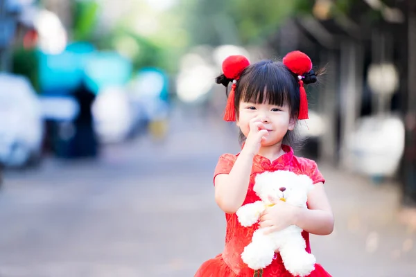子供は赤い中国の服を着て立って かゆみから鼻を引っ掻いています 可愛い子が白いテディベアを持ってる 小さな笑顔甘い女の子 4歳のアジアの子供たち — ストック写真