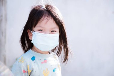 Gizli çocuklar koronavirüs hastalığının yayılmasını önlemek için tıbbi maske takarlar (Covid-19). Sabah yürüyüşü için pijama giyen bir çocuk konut alanında yürüyor. Kameraya bakan tatlı kız..