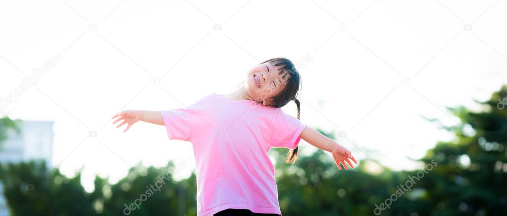Happy little Asian cute girl spread both arms and tilted neck. Sweet smile child holding hands up. Looks at camera. Children do flying poses with sky. Active kid wearing pink shirt aged 3-4 years old.