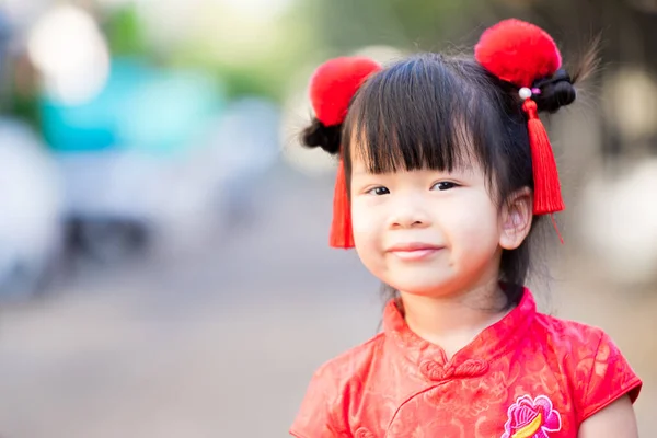 アジアの少女は 中国の旧正月を祝うために 先祖伝来の伝統によると 赤い房で 赤いChongsamに身を包んだとふわふわの髪のクリップで飾られた 幸せな子供の笑顔甘い — ストック写真