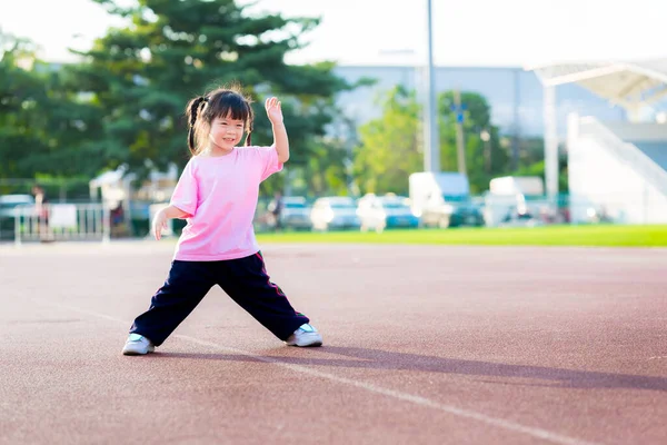 アジア系の少女が運動場で運動している 子供たちは離れて足と腕を体を暖めるために提起立っている ピンクのシャツを着たかわいい子供の甘い笑顔 幸せな子供3 — ストック写真