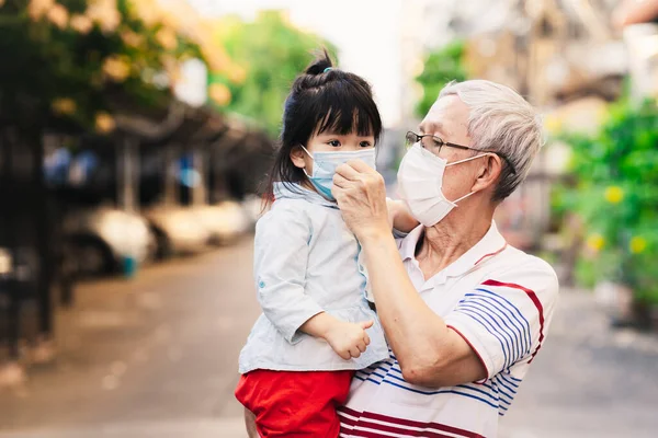 Grandpa wear face mask to kids for protect corona virus pandemic  outside home. Family always use medical mask for protect covid-19 disease for family health care for preschool and elderly from virus.