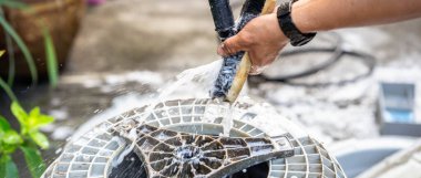 Bir insanın eli, çamaşır makinesinin davulunu temizlemek için fırçaladığı siyah kıllı ahşap bir fırçayı tutuyor. Yüksek basınçlı hortumun başı, su eşit bir şekilde dağılana kadar çalıların üzerinde durur..