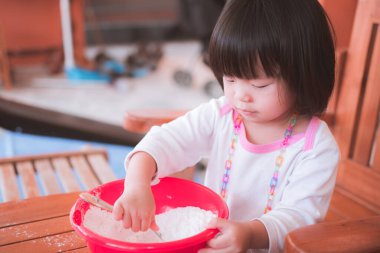 2-3 yaşlarında küçük bir Asyalı kız. Patongko aktiviteleri için un üretiyor. O, büyük bir kasede karıştırmak için dikkatle bir kaşık kullanıyordu. Çocukların evde eğlenceli aktiviteler yapmaları fikri.