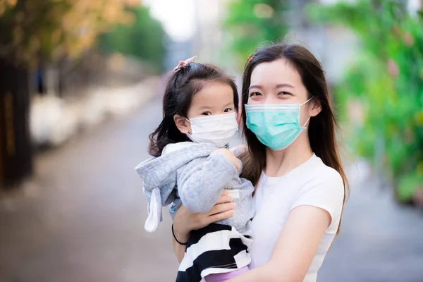 Asian family and adorable child girl wearing medical face masks on public roads. Mother and kid wear mask protection corona virus during outbreak pneumonia scourge. Face mask for protect pm2.5 dust.