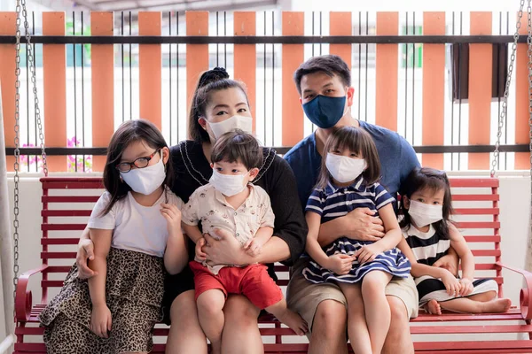 Parent and son, daughters wear mask clothes and medical masks. They sat on swing in front of house. Stay at Home in Corona virus epidemic situation. Asian family New Way of Life (New Normal) concept.