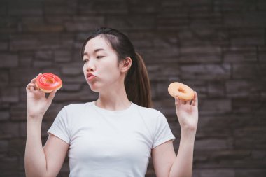 Yaz mevsiminde gülümseyen güzel bir kadının komik portresi. Yüzüne donut tutan biri. Koyu duvar mor arkaplanda.