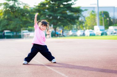 Spor alanında egzersiz yapan aktif bir kız. Mutlu çocuk tatlı tatlı gülümsedi ve mutlu bir şekilde güldü. Çocuklar akşamları spor yapar. Saçta güneş ışığı. Çocuğun elleri titreyerek güçlü bir vücudu var. Bebek 3-4 yaşında..
