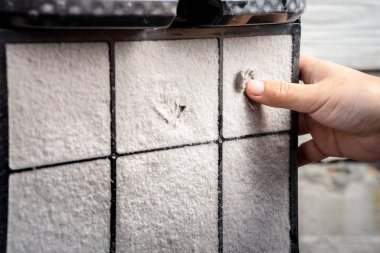 PM2.5 hava temizleyicisinin kalın tozlu filtresi bir çarşaf oluşturur. Bir kişinin eli onu temizlemek için toz örtüsünü kaldırmaya çalıştı..