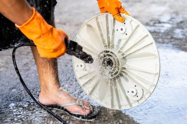 Yüksek basınçlı hortum kullanan kişi otomatik çamaşır makinesinin tabanını duruluyor. Küvetin arkasını yıka..
