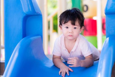 Sevimli çocuk mavi kaydırma hareketini yaptı. Bebekler oyun bahçesinde oynarlar. Yaz ya da bahar aylarında. Çocuk kameraya bakıyor, 1-2 yaşında..
