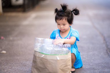 Çocuk geri dönüşüm için temiz plastik şişeleri ayırıyor. Çocuklar temiz plastik şişeleri açık kahverengi kağıt torbalarda saklarlar. Atık geri dönüşümü yoluyla küresel ısınmayı azaltma kavramı. Bebek 2-3 yaşında..