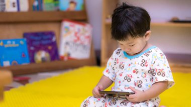 Asyalı erkek bebek cep telefonunda çizgi film izlemek için başını eğdi. Küçük çocuklar ve animasyon medyasının kullanımı. Bulutlu bir günde. Çocuk 1-2 yaşında..