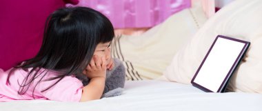 Yumuşak beyaz şiltede tabletten çizgi film izleyen bir kız. Çenesini destekleyen 4 yaşında bir çocuk. Çocuk çenesini gri bebeğe takmış, dokunmatik ekranda video izliyor. Teknolojinin sınır kullanımı kavramı.