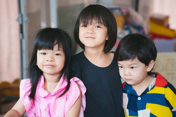 Three sibling held a photo together. Asian cute girl smiles sweetly, the boy does not look at the camera. Adorable children aged 2-6 years old. cousin.