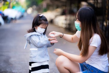 Aile halka açık yerlerde maske takar. Kız elini annesine açtı. Virüs ve bakterilerden ellerini yıkamak için alkol sıktı. Koronavirüsün ve PM2.5 toksik tozunun yayılmasını önle, hava kirliliği sorunu.