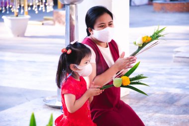 Maske takan aile tapınaktaki rahiplere saygılarını sunacak. Anne ve kızın elleri çiçek tutuyor. Virüsün ve hava kirliliğinin yayılmasını önlemek için. Çin Yeni Yılı 'nda başarılar dile getir..
