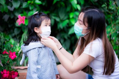 Koronavirüs ve PM2.5 toksik tozunun yayılmasını önle, hava kirliliği sorunu kavramı. Anne, kovid 19 ve hava kirliliğini önlemek için kızına tıbbi yüz maskesi takıyor. Aile virüsü korur.