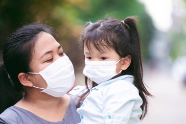 Aile halka açık alanlarda COVID-19 yayılmasını önlemek için maske takıyor. Anne, maske takmak istemediği için ağlayan kızını teselli ediyor. Anne kucağında çocuk gözyaşlarıyla ağlıyor gözlerinden yaşlar akıyor..