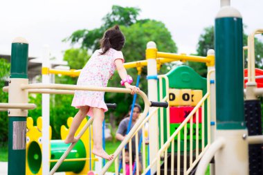 Oyun parkına tırmanan Asyalı güzel bir kızın arkadan görünüşü. Mutlu sağlıklı çocuk egzersiz yapmayı seviyor. Yaz ya da bahar aylarında. Elbise giyen çocuk 5-6 yaşlarında..
