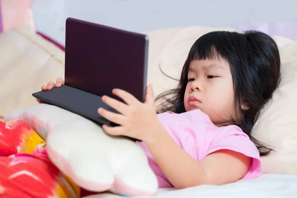 Gadis Asia Yang Lucu Berbaring Menonton Kartun Dengan Tablet Hitam — Stok Foto
