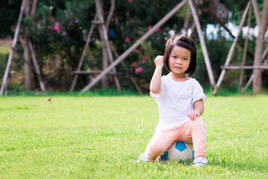 4 yaşındaki bir çocuğun portresi. Mavi-beyaz topun üzerinde oturan mutlu Asyalı kız. Sevinç gösteren aktif bir çocuk. Sağlıklı bebek konsepti. Yaz zamanı yeşil çimlerde spor.