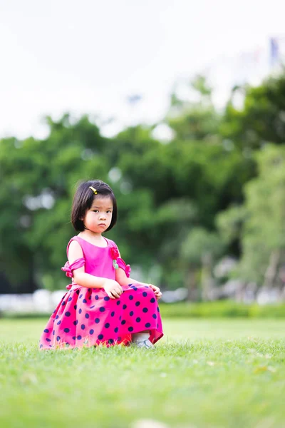 垂直图像 亚洲女婴坐在绿草中 闷闷不乐的孩子孩子们穿着深红色的衣服 5岁女性 — 图库照片