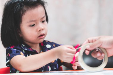 Asyalı çocuk çift taraflı bandı dikkatlice kesmek için pembe makas kullanıyor. 4-5 yaşındaki bir kız, aletleri dikkatli kullanmayı öğreniyor..