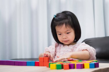 Oyun odasında tahta bloklarla oynayan çocuklar. Şirin küçük kız uzun sıralar halinde oyuncaklar düzenliyor. 4-5 yaşlarındaki Asyalı çocuk.
