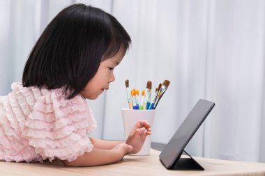 Sosyal Uzaklık Öğrenme Konsepti. Online eğitim. Dokunmatik ped kullanan mutlu bir kız. Çocuk parmağıyla dijital resim yapıyor. 4-5 yaşlarındaki öğrenci.