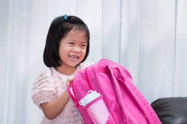 Okul konseptine geri dönelim. Mutlu öğrenci kız okul malzemeleriyle pembe sırt çantası hazırlıyor. Çantada yedek olarak tıbbi maske bulunur..