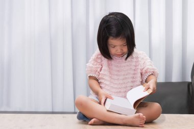 Asyalı bir çocuk evindeki ahşap masada oturup büyük bir kitap okuyor. Mutlu kız tatlı gülümsemesi. Çocuk elinde tuttuğu yeni kitaba hayret etti. 4-5 yaşlarındaki çocuklar.
