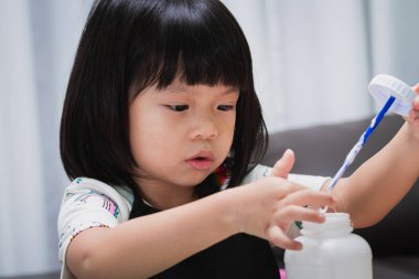 Yüzü kapalı kız sınıfta zanaat öğreniyor. Anaokulu öğrencisi, icat için yapıştırıcıya dokunuyor. Eğlence projeli anaokulu çocuğu. 4-5 yaşlarında siyah önlük giyen bir bebek..