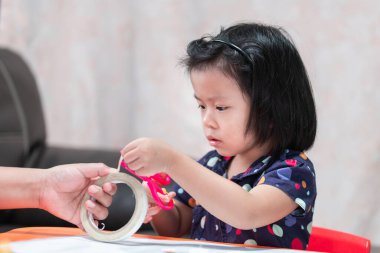 Çocuk kağıt yapıştırıcısı kesmek için pembe makas kullanıyor, tatlı kız öğretmenleri okula göndermek için el işi yapıyor. Çocuk 4-5 yaşlarında. Kaset bir yetişkinin elinde..