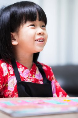 Dikey görüntü. Asyalı öğrenci kız tatlı gülümsemesinin portresi. Siyah önlük giyen küçük bir sanatçı. Çocuk suluboya resim yapıyor..