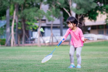 Çocuk yeşil plastik raketi badmintonla tekmeleyerek eğleniyor. Yeni bir şeyler öğren ve çabalarınla gurur duy. Spor zamanı..