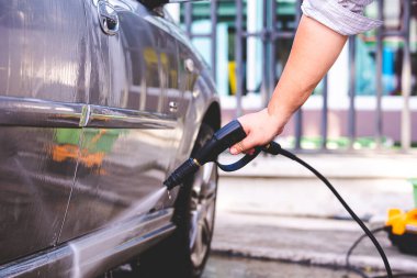 İnsan eli, arabayı temizlemek için yüksek basınçlı siyah hortumlar kullanır..