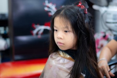 Kuaförde saç kesiminden sonra yüzünde ciddi bir ifadeyle oturan genç bir Asyalı kız. Çocukluk sabrı, tımar seansının bitmesi ve güzellik salonunda çocuk deneyimi..