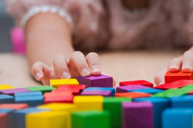 Close-up of a child's hands playing with colorful wooden blocks on a table. Concept of early childhood development, creative learning, educational toys, and fine motor skills in a preschool setting.