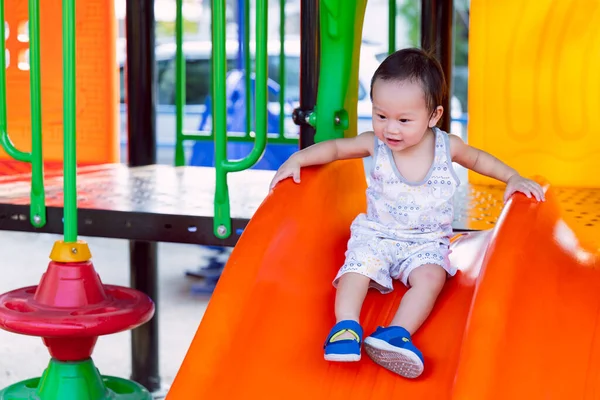 Neşeli çocuk, açık hava oyun parkında canlı bir turuncu kaydırak üzerinde başarıyla kayıyor. Aktif açık hava oyunlarında çocukluk başarısı, fiziksel aktivite ve saf mutluluk kavramı.