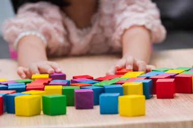Close-up of a child's hands playing with colorful wooden blocks on a table. Concept of fine motor skills development, early childhood education, and creative learning through tactile play.