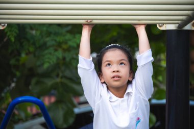 Açık hava çocuk parkında maymun parmaklıklarından sarkan kararlı bir genç kız. Fiziksel bir meydan okuma, üst vücut gücü gelişimi ve aktif çocukluk tatili sırasında odaklanmak..