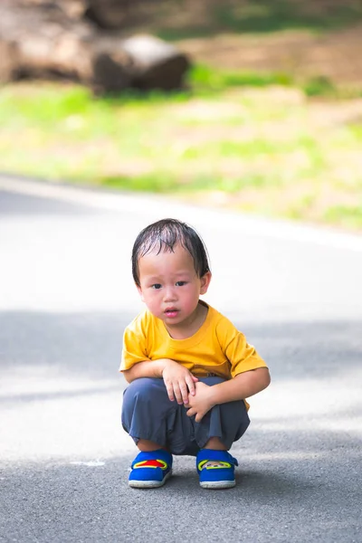 Parlak sarı tişörtlü, mavi ayakkabılı, parkta çömelmiş şirin bir çocuk. Bir anlık merak, açık hava keşfi ve güneşli bir bahçe ortamında samimi bir çocukluk hayatı yakalamak..